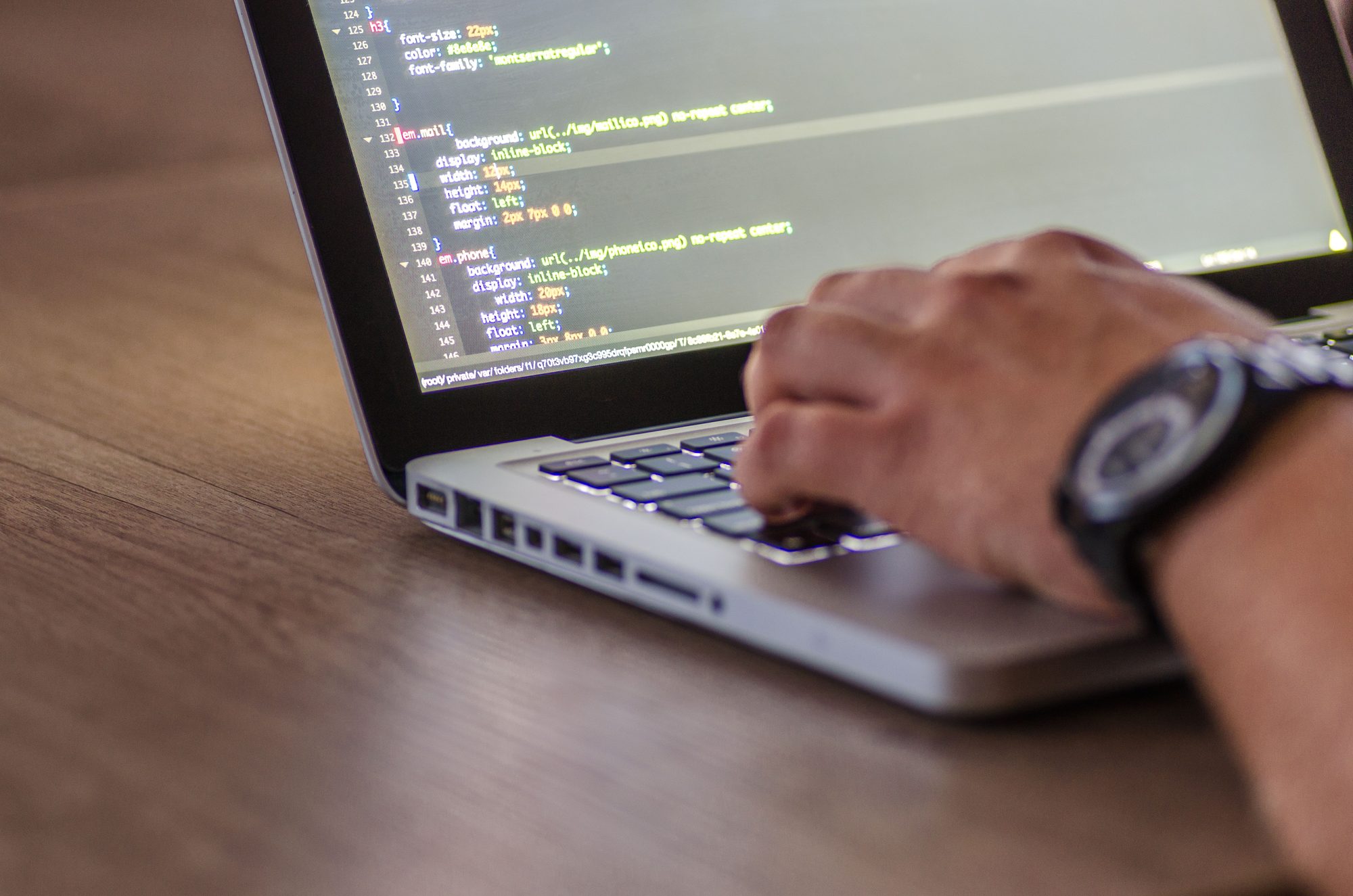 Hands on a laptop keyboard with programming code on the screen